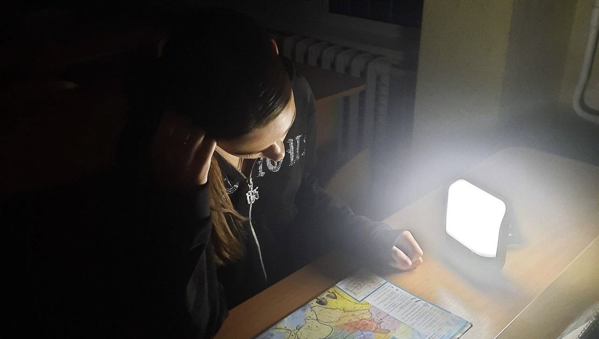 A student in a shelter in Kyiv using a BRIGHT Sol Mid Capacity solar lamp to study a map during a power outage.