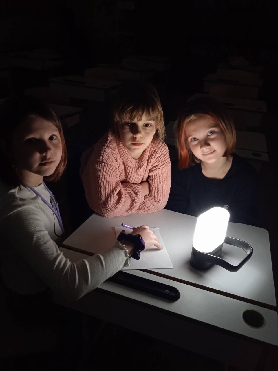 Students pose in front of a Sol Mid Capacity solar lamp on its medium light setting in a dark classroom