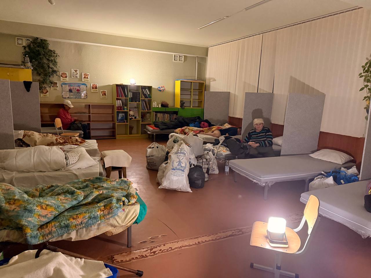 Evacuees sit in a softly lit room at the Lozova Transit Centre, illuminated by a Sol solar lamp.
