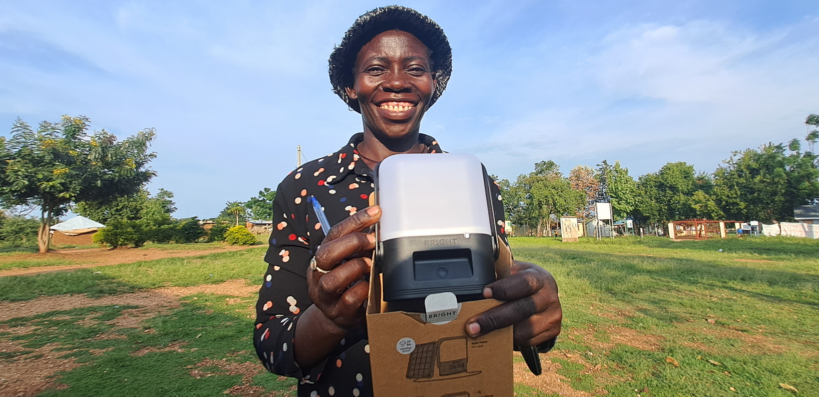 A refugee in Bidibidi settlement holding a portable Sol solar lamp distributed for household lighting and everyday use.