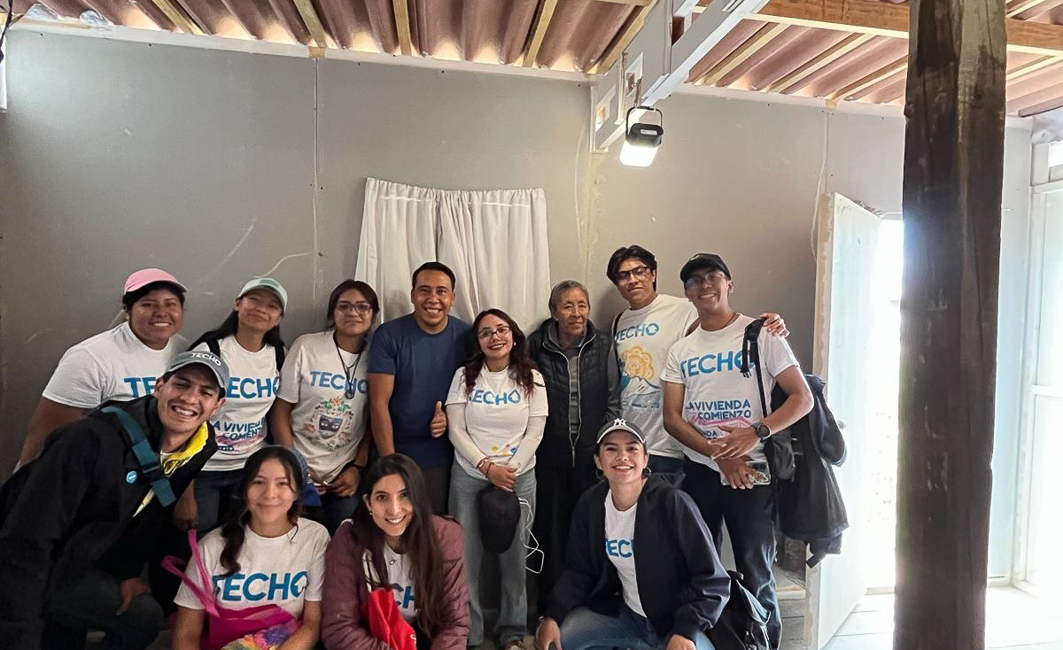 A group of TECHO Mexico representatives standing together inside a shelter after mounting a Sol Mid Capacity solar lamp for indoor lighting.